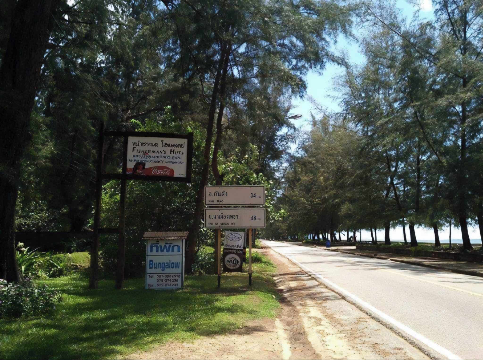 Un cartel al borde de la carretera con varios anuncios, incluyendo uno de cabañas y otro de Cabañas Fisherman's Huts.