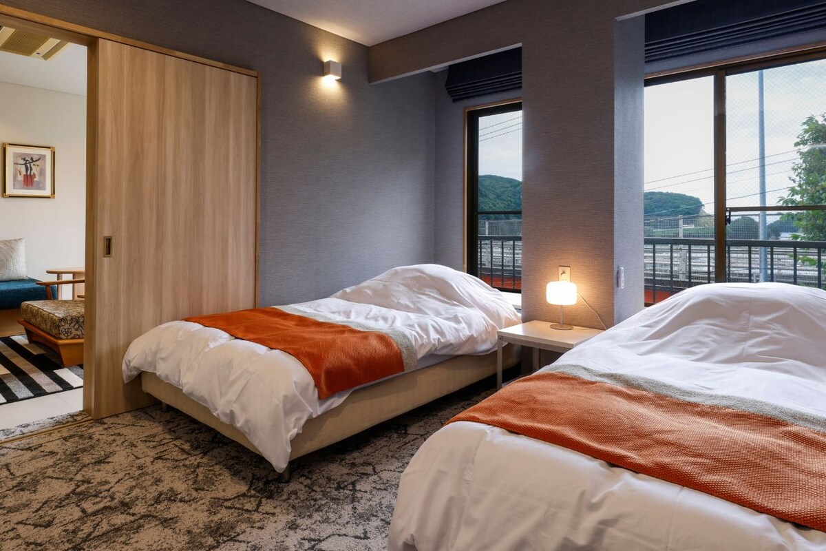 A hotel room with two beds, a sofa, a small table, and a view of a bridge.