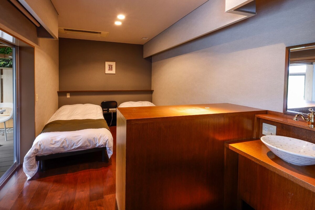 A modern hotel room with a wooden bed, a wooden vanity with a sink, and a sliding glass door to a balcony.
