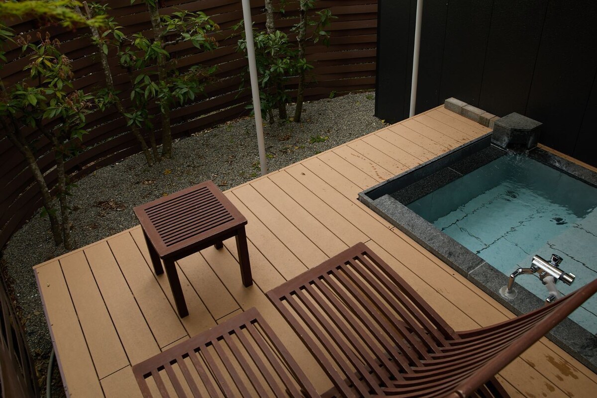 A wooden deck with a hot tub, two wooden chairs, and a small table.