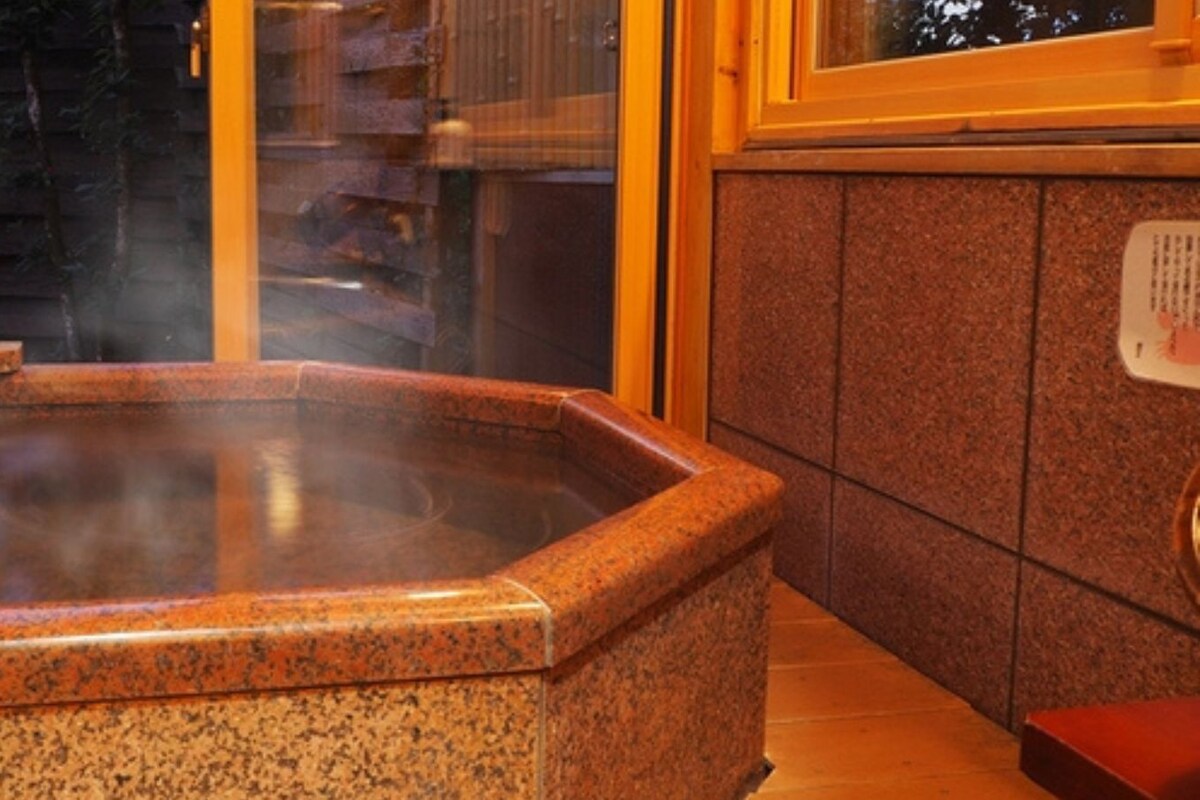 A hot tub with a stone exterior, a wooden bench, and a tiled wall with a control panel.