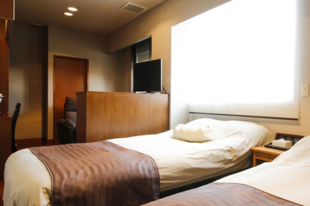 A hotel room with two beds, a TV, and a window.
