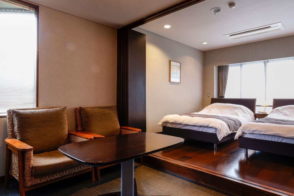 A hotel room with two beds, a small table, and a chair.