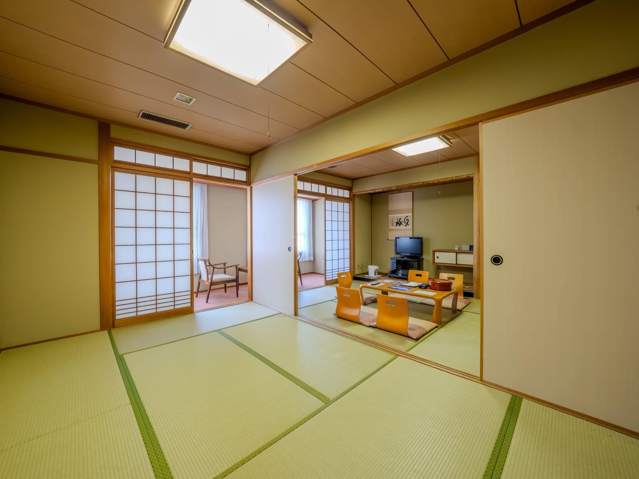 A traditional Japanese room with tatami flooring, a low table with cushions, a television, and sliding doors.