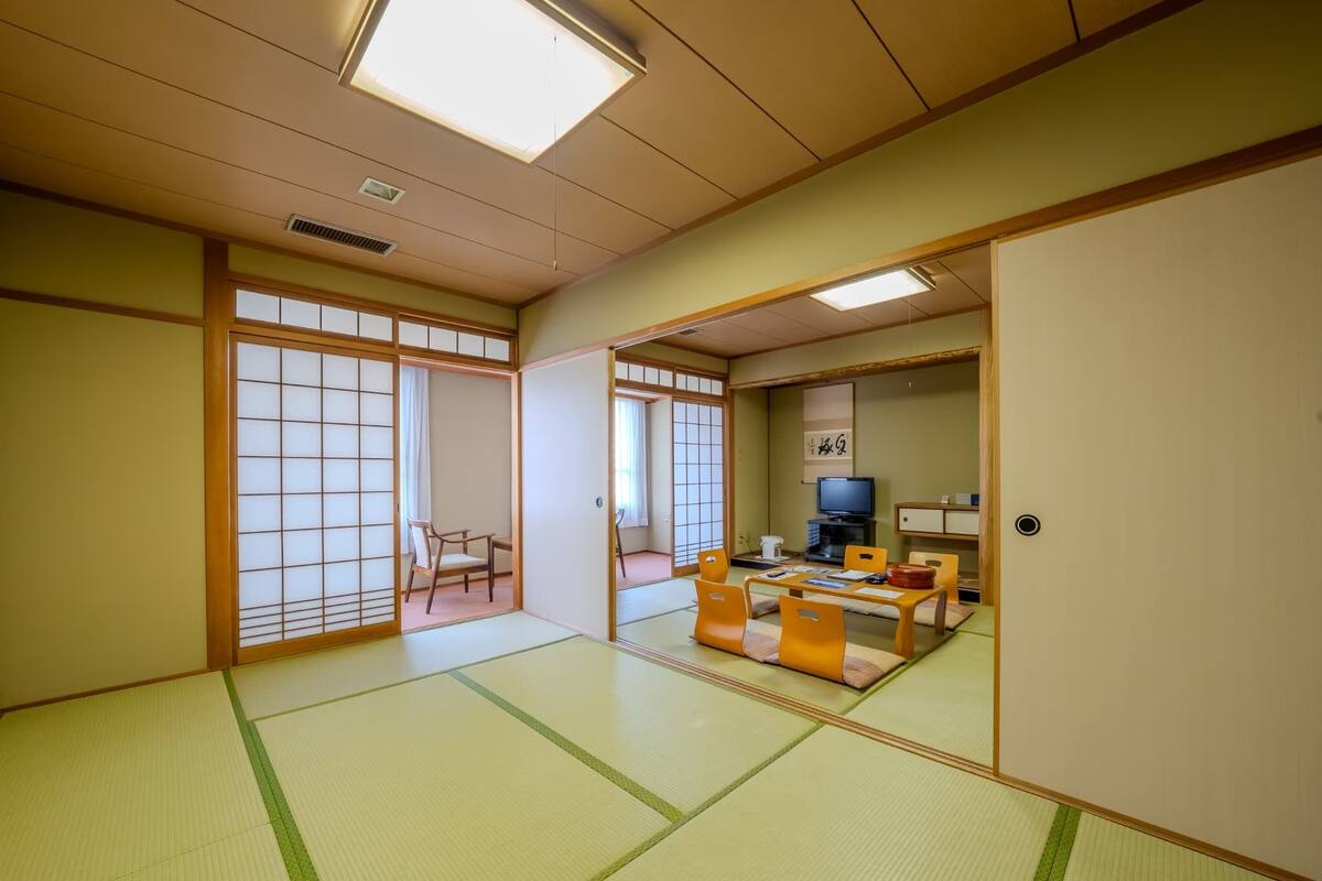 A traditional Japanese room with tatami flooring, a low table with cushions, a television, and sliding doors.