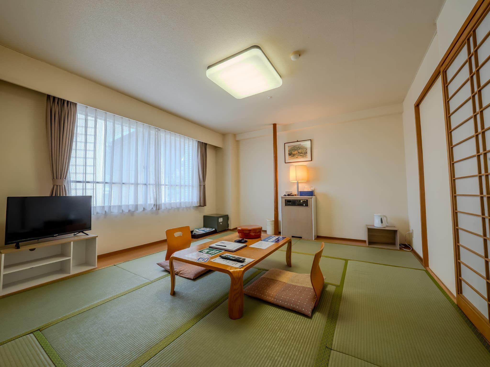A room with tatami mats, a television, a desk with a lamp, and a futon bed.