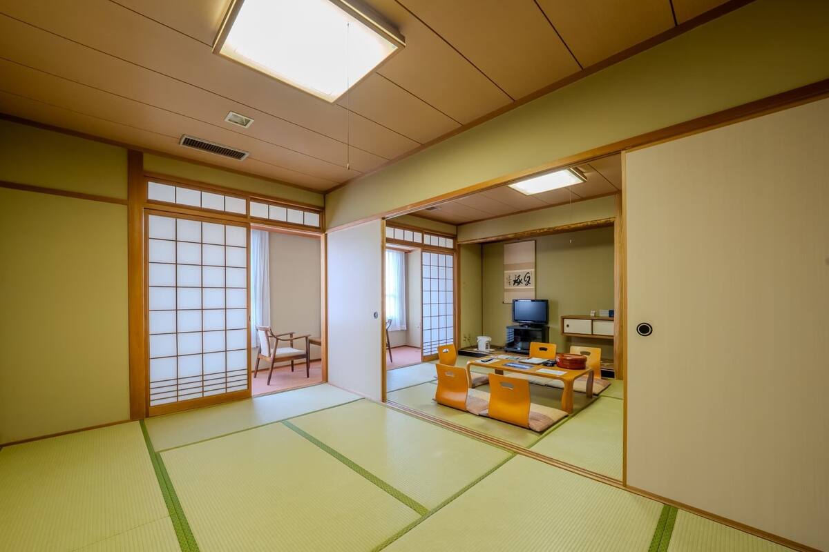 A traditional Japanese room with tatami flooring, sliding doors, a television, and a table with chairs.