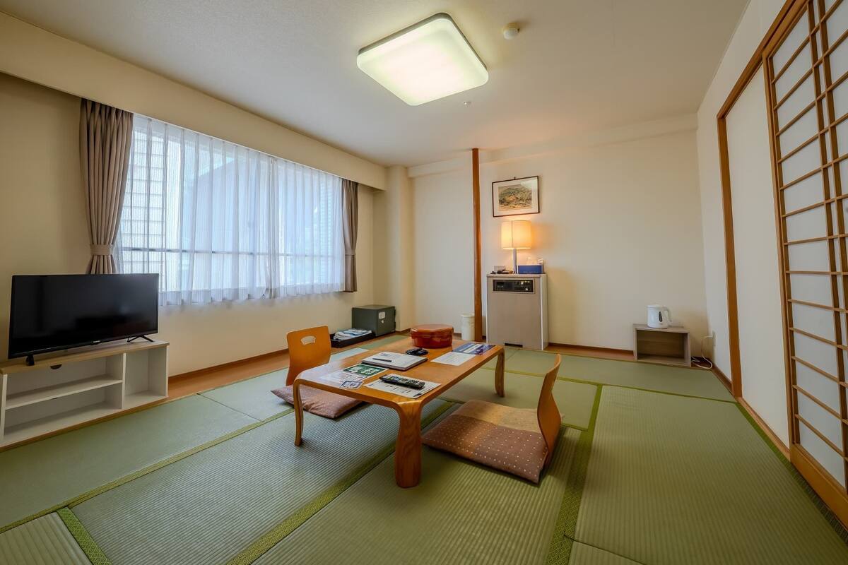 A room with tatami mats, a television, a desk with a lamp, and a traditional sliding door.
