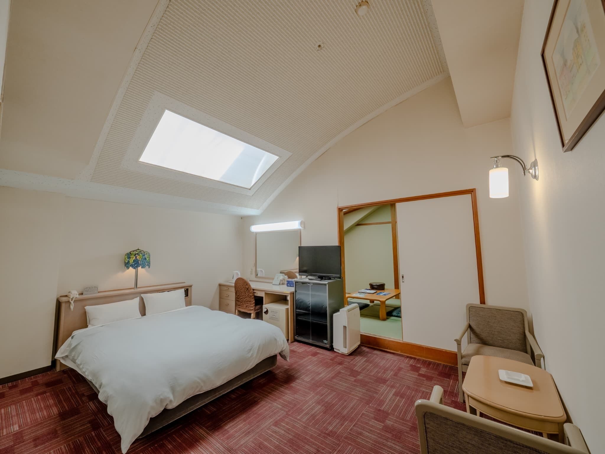 A hotel room with a bed, desk, chair, and a large mirror.