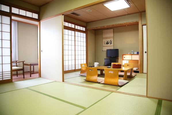 A traditional Japanese room with tatami flooring, a low table with cushions, and sliding doors. - Hotel Luna Park (Matsuyama)