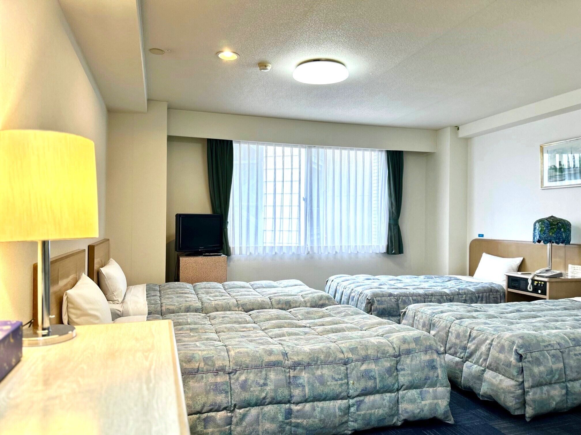 A hotel room with two beds, a desk, a TV, and a window with curtains.