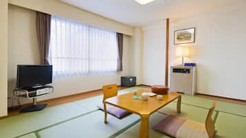 Une chambre d’hôtel équipée d’une télévision, d’une table avec une théière et des tasses, d’un canapé et d’une fenêtre avec des rideaux.
