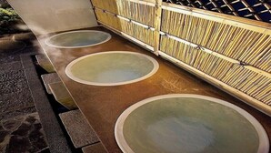 Ein traditionelles japanisches Onsen mit drei Thermalbädern, einem Holzzaun und einem Schild mit japanischen Schriftzeichen.