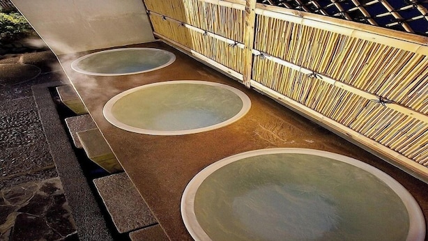 Un onsen japonais traditionnel, avec trois bains d’eau chaude, une clôture en bois et une enseigne avec des caractères japonais.