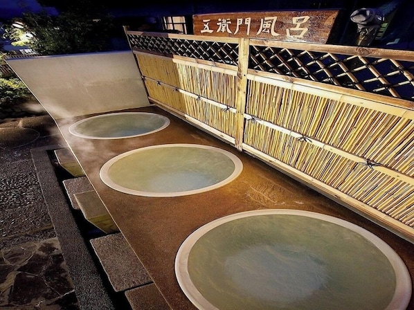 A traditional Japanese onsen with three hot water baths, a wooden fence, and a sign with Japanese characters. - Hotel Luna Park (Matsuyama)