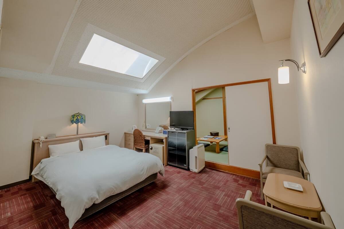 A hotel room with a bed, desk, chair, and a large mirror.