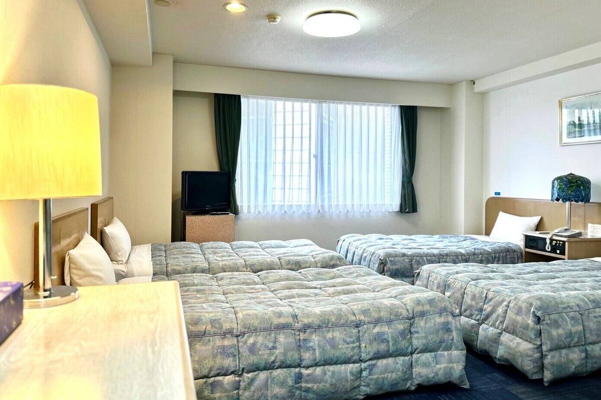 A hotel room with two beds, a television, a desk, and a window with curtains.