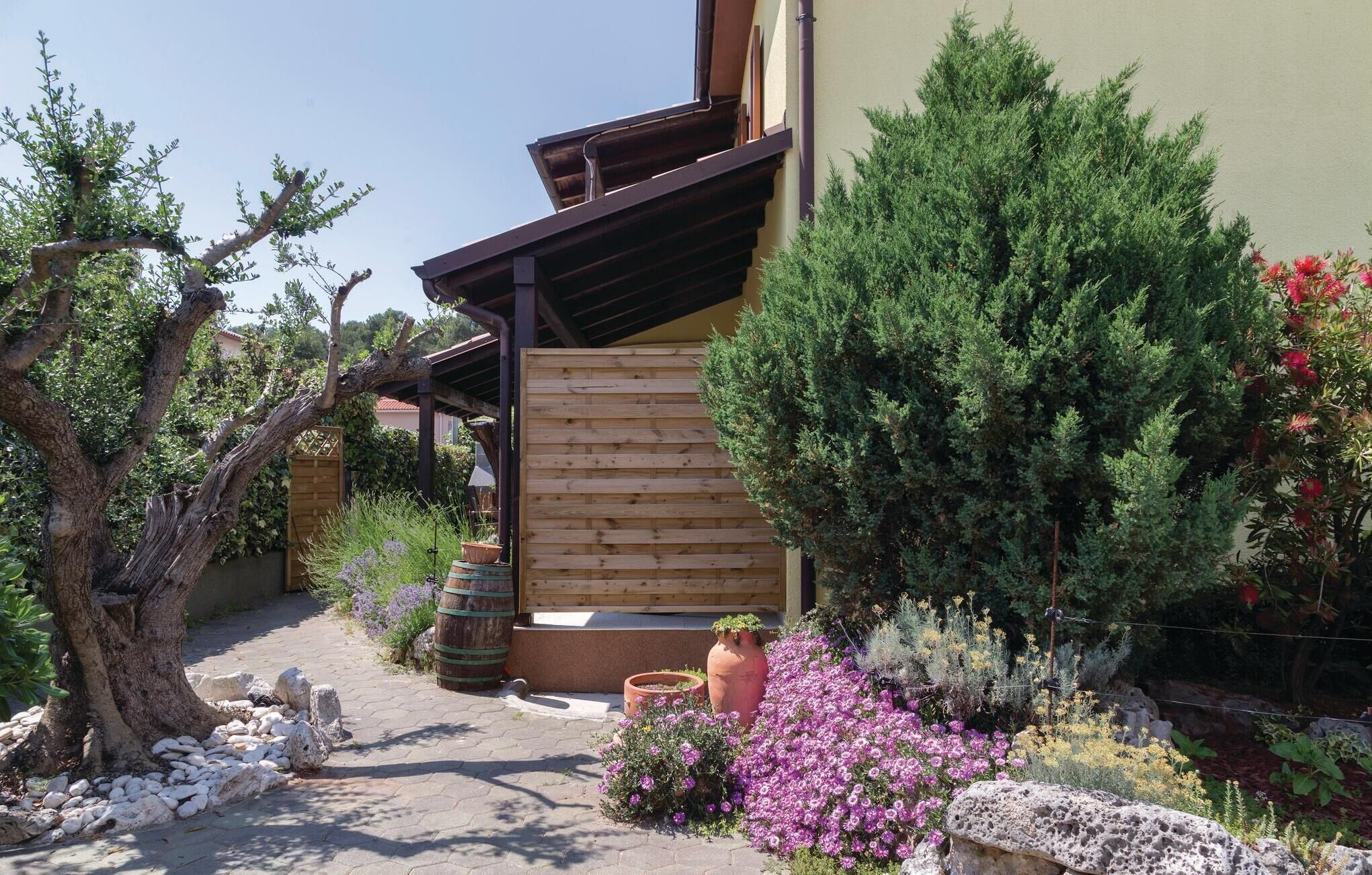 A garden with a wooden pergola, potted plants, and a variety of shrubs and flowers.