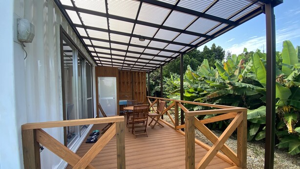 A wooden deck with a glass ceiling, surrounded by lush greenery. - Bise House (Motobu)