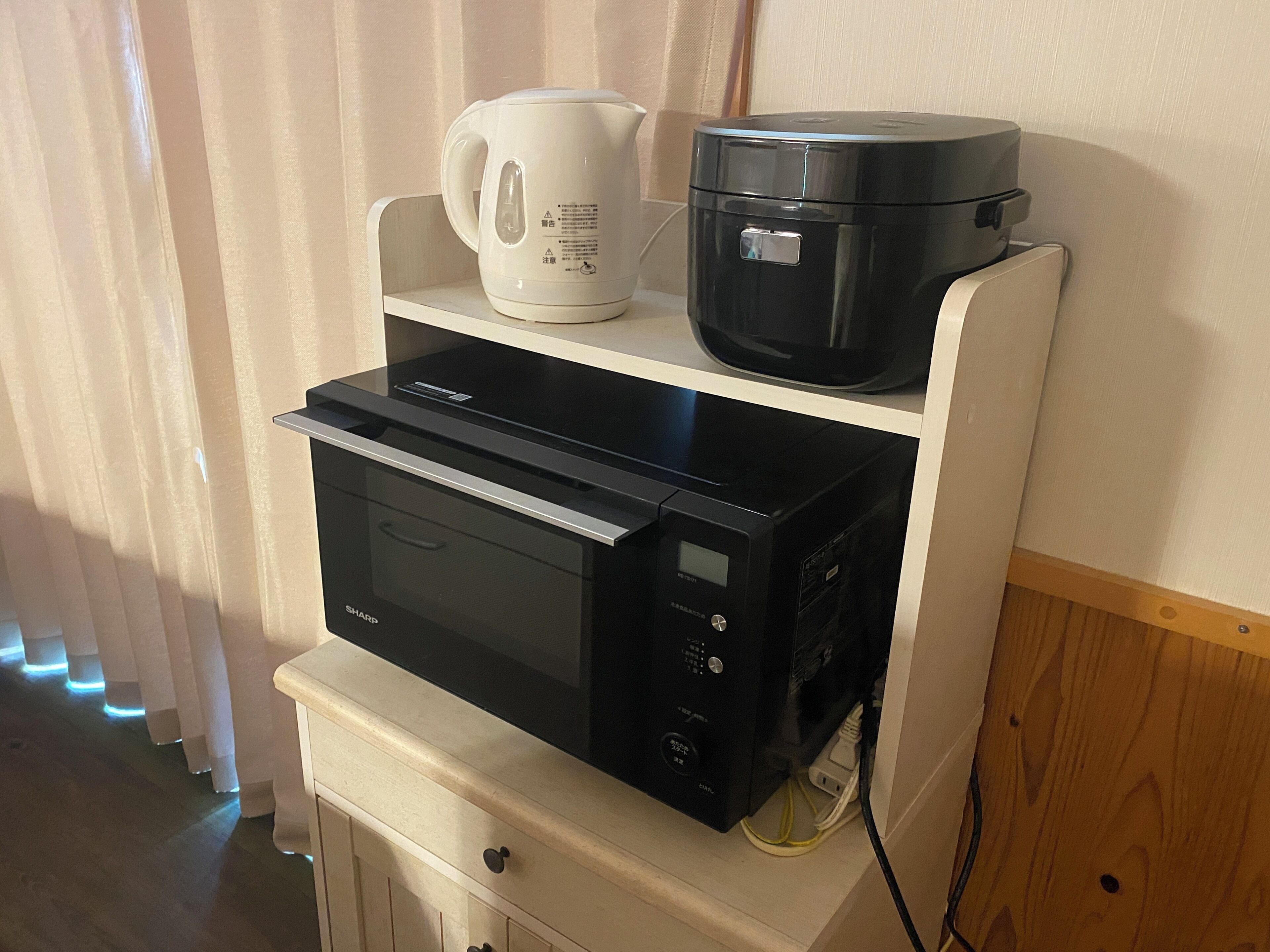A kitchen area with a microwave, a coffee maker, and a rice cooker on a white cabinet.
