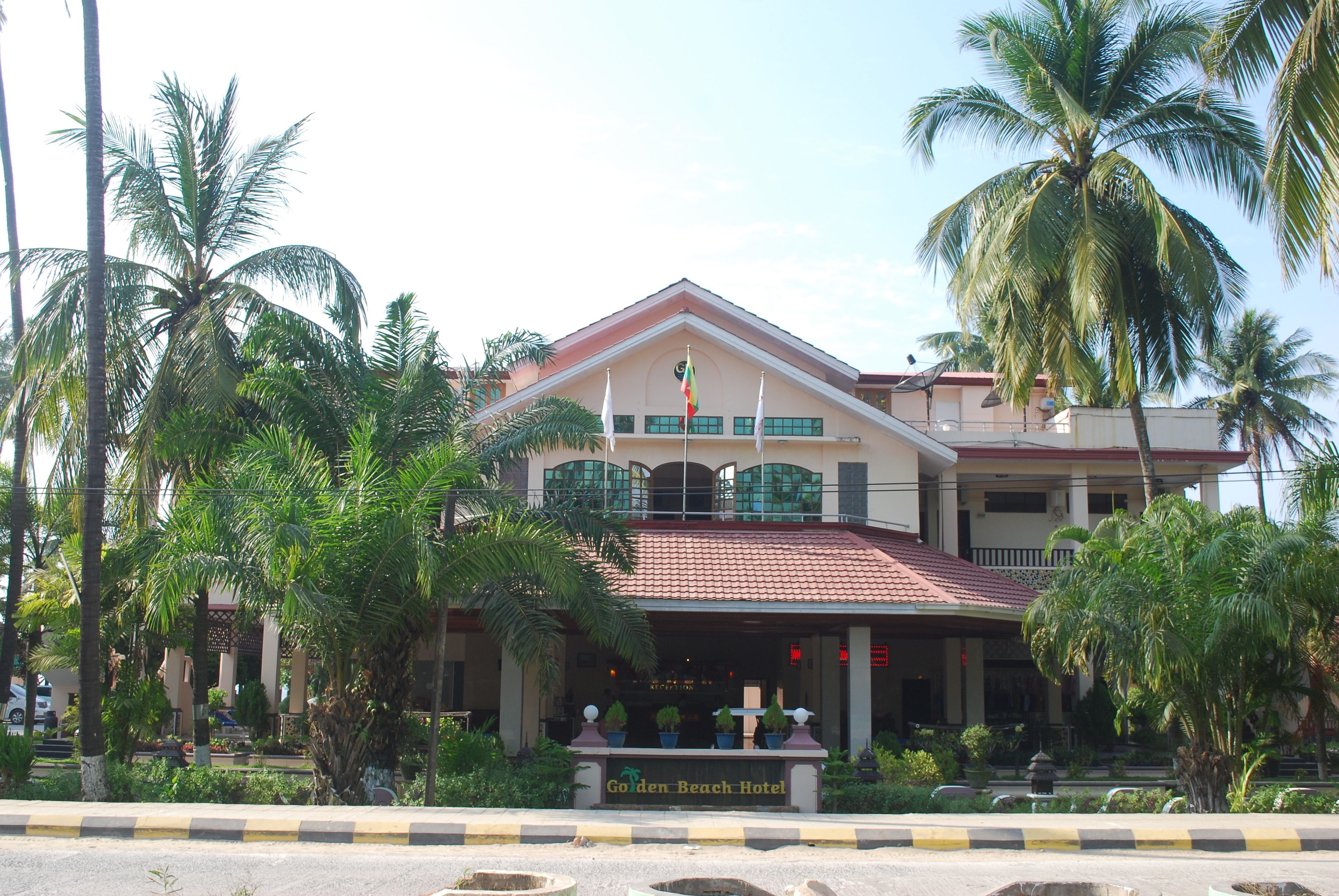 Un hotel con tetto in tegole rosse, un balcone e un cartello con la scritta 'Golden Beach Hotel'.
