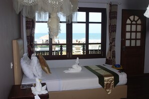 A hotel room with a bed, a window with a view of the beach, and a door.