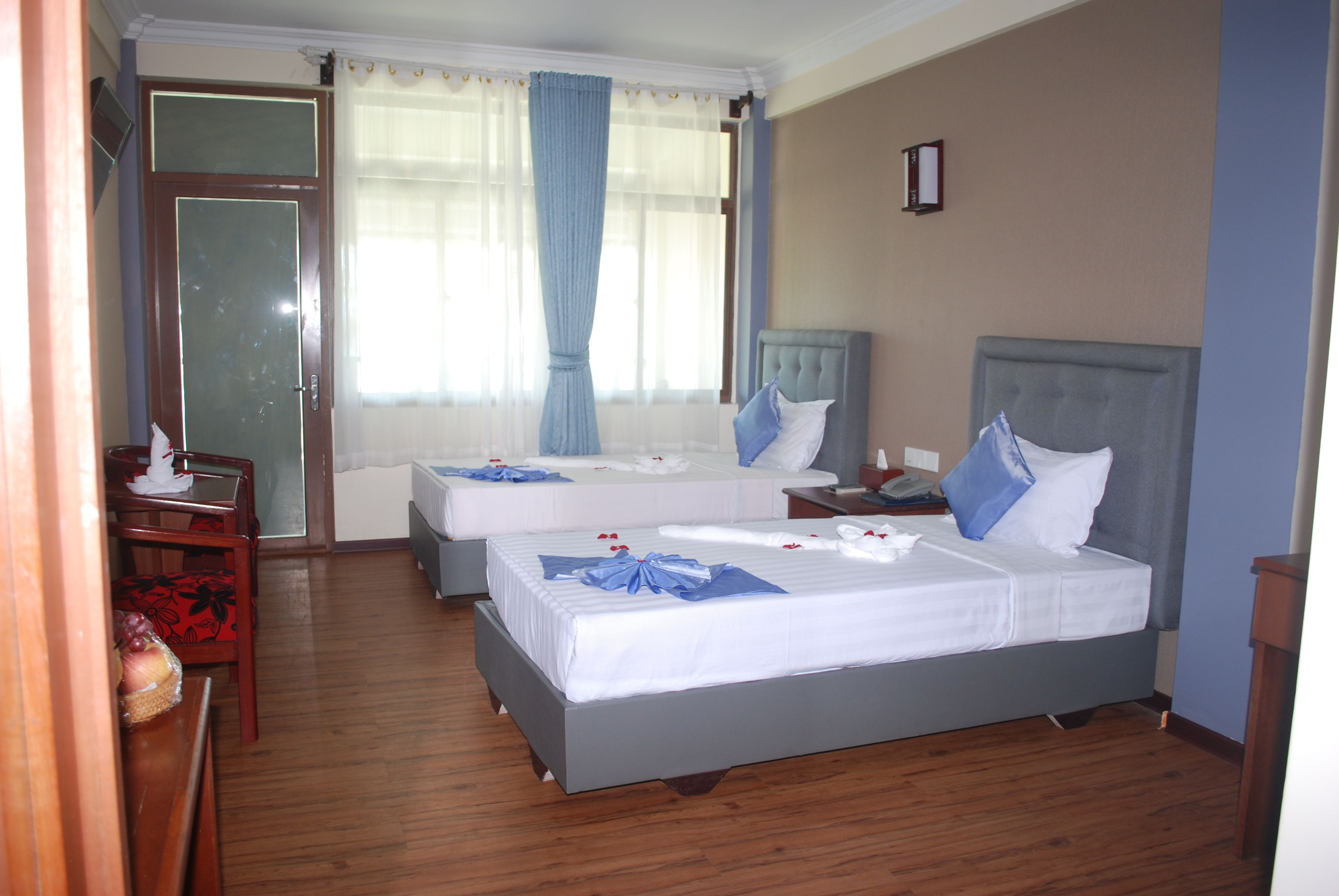 A hotel room with two beds, a wooden floor, a desk, and a chair.