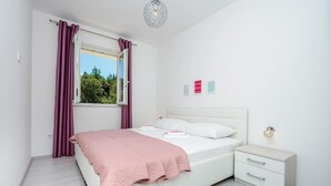 A bedroom with a bed, a nightstand, a window with curtains, and wall art. - Amazing apartment in Cavtat with house sea view (Cavtat)