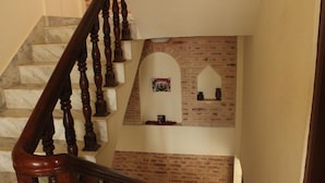Una escalera con barandilla de madera y peldaños de mármol, que conduce a una habitación con pared de ladrillo y una pequeña ventana apuntalada.