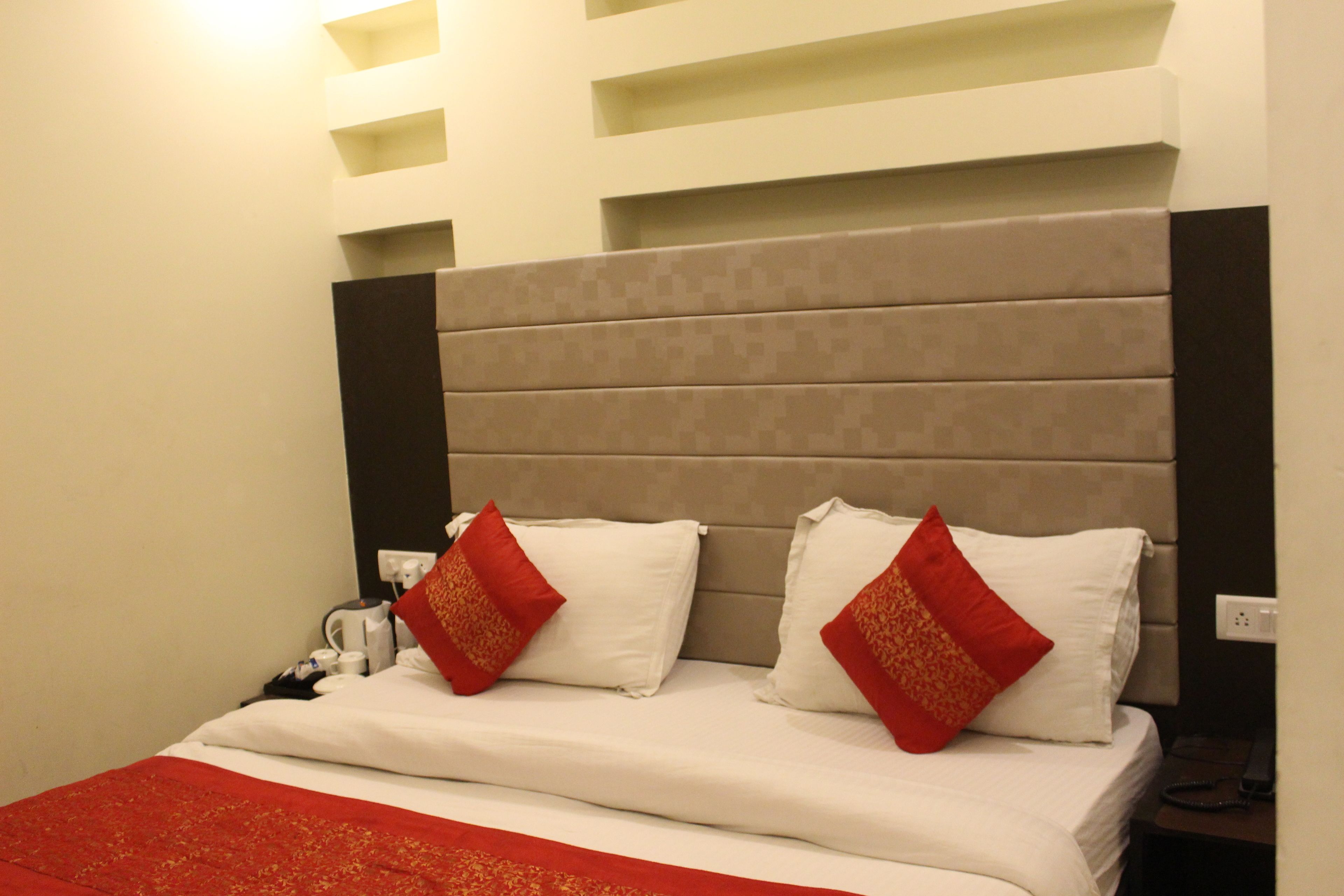 A hotel room with a bed, two red pillows, a white bedspread, and a red runner.
