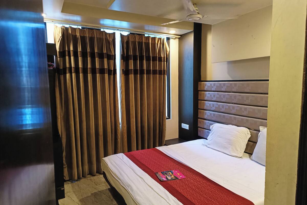 A hotel room with a bed, curtains, a ceiling fan, and a window with curtains.
