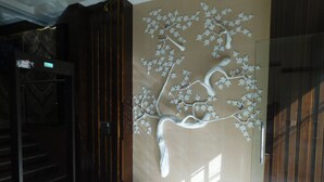 A modern interior with a glass door, a wooden door, and a wall with a tree mural. - Hotel Gauranga Nearest New Delhi Railway Station (New Delhi)