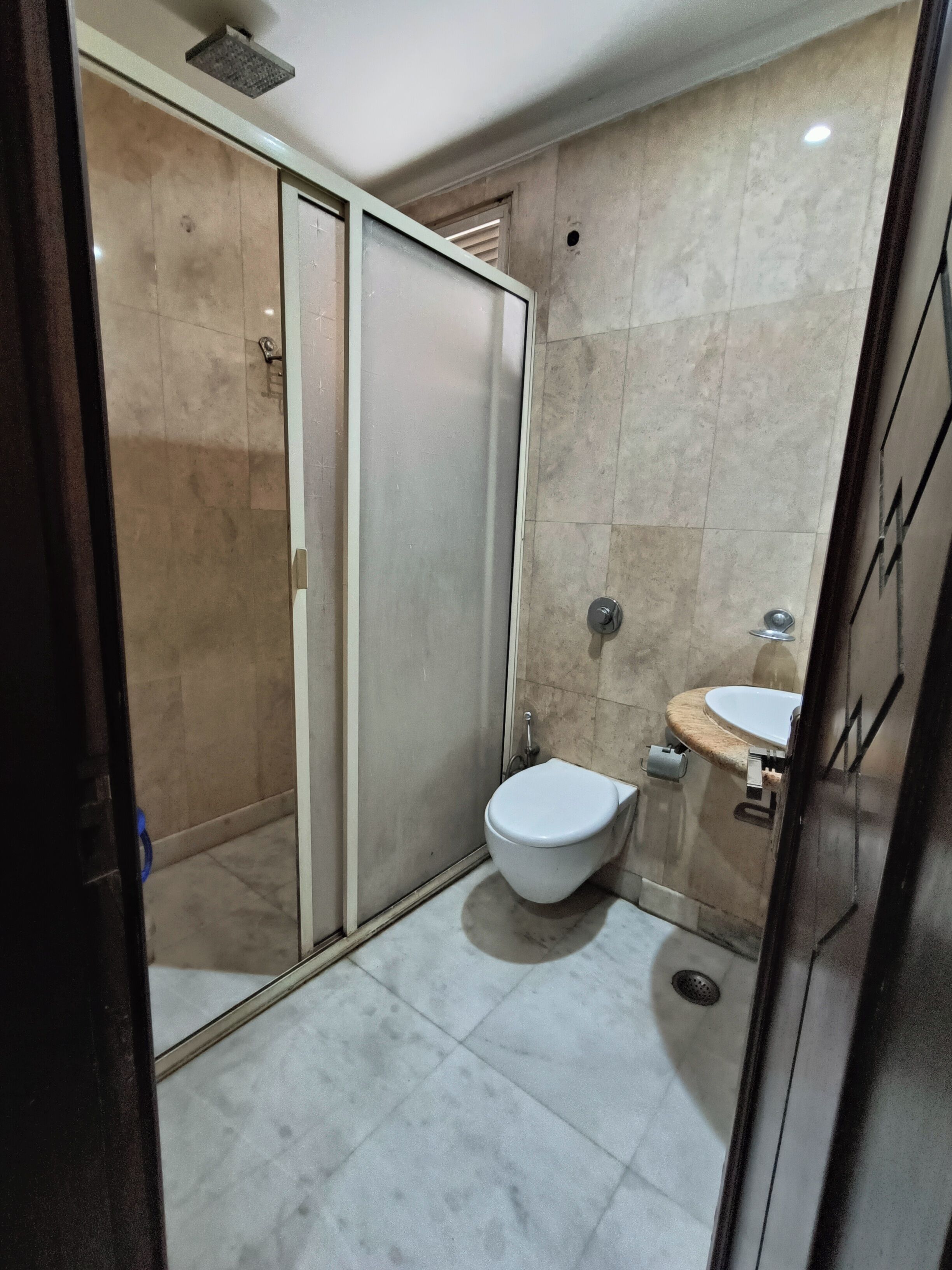 A bathroom with a glass shower enclosure, a toilet, and a sink.