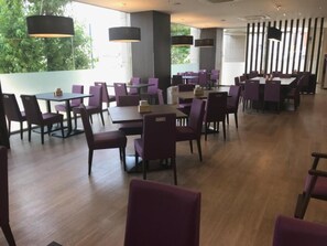 A spacious dining area with tables and chairs, large windows, and hanging light fixtures.