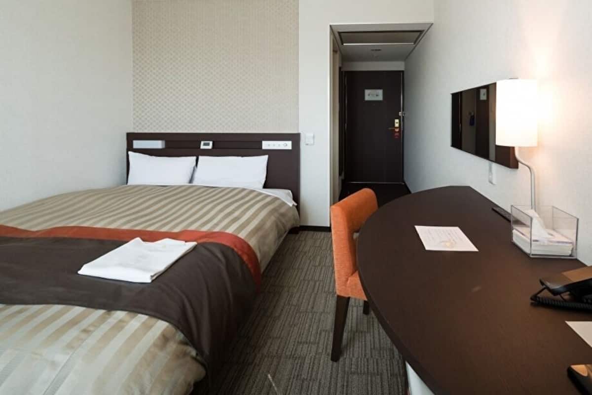 Ein Hotelzimmer mit Bett, Schreibtisch, Stuhl, Lampe und einer Tür.