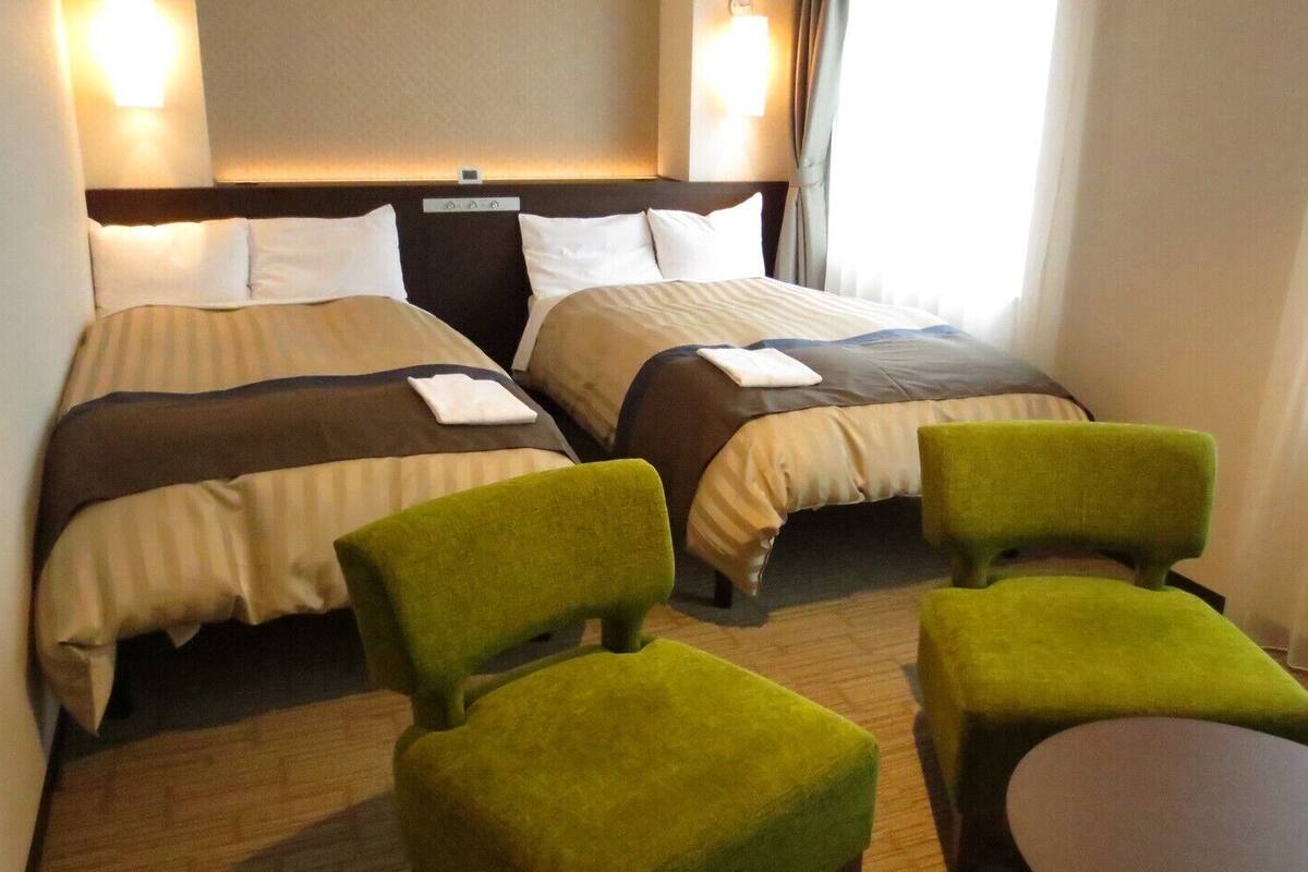 Ein Hotelzimmer mit zwei Betten, einem Kopfteil, einem kleinen Tisch und zwei grünen Sesseln.
