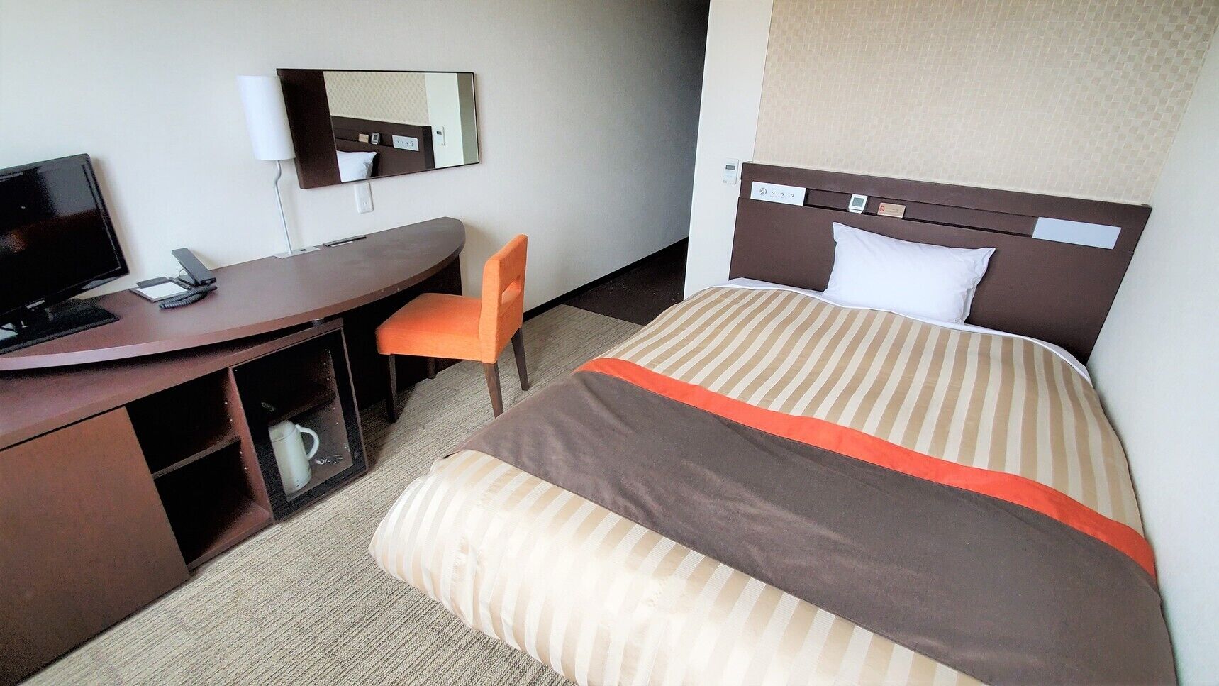 A hotel room with a bed, a desk, a chair, a television, and a mirror.
