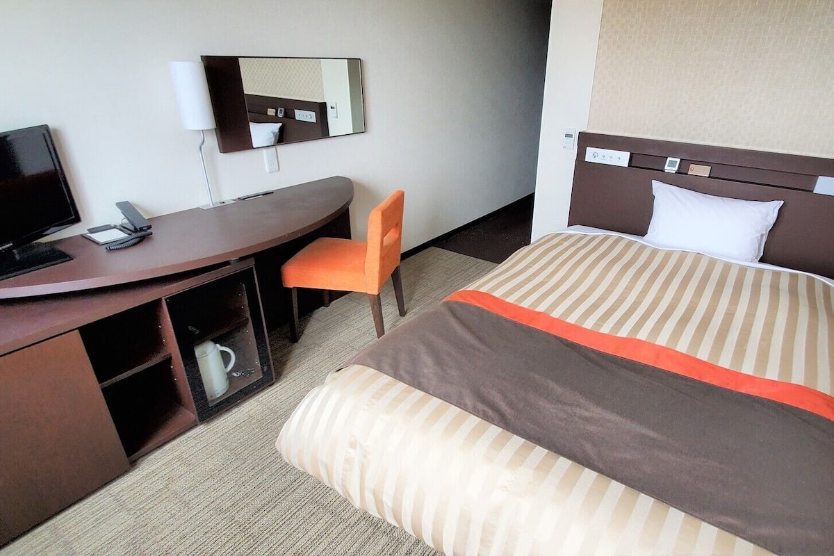 Ein Hotelzimmer mit Bett, Schreibtisch, Stuhl, Fernseher und Spiegel.