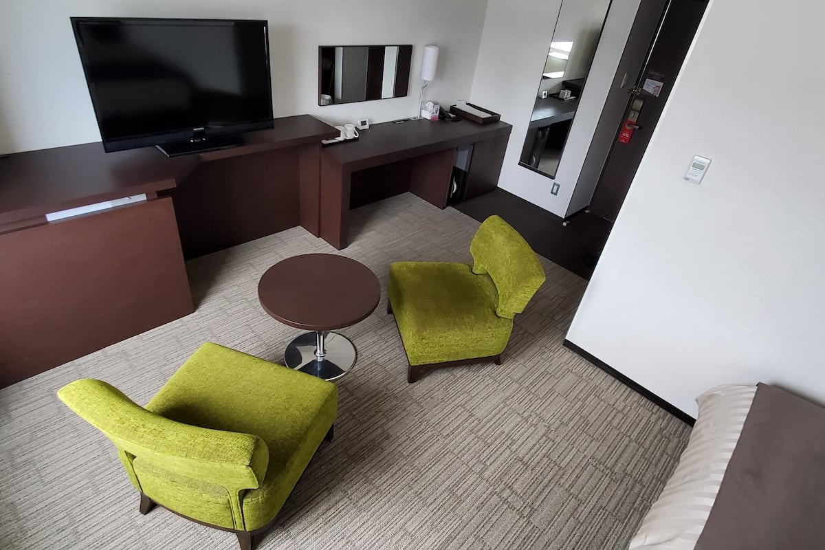 Ein Hotelzimmer mit Flachbildfernseher, Schreibtisch, Sessel und einem runden Tisch.