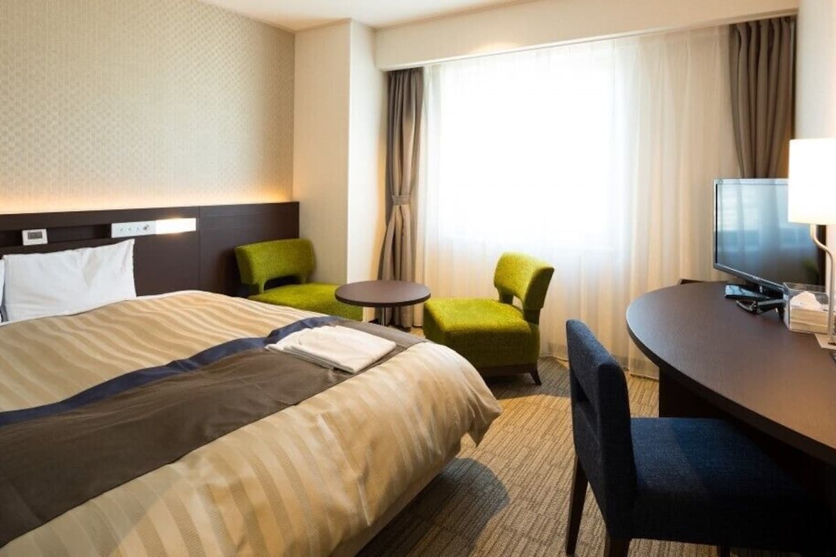 Ein Hotelzimmer mit einem großen Bett, einem Schreibtisch mit Stuhl, einem Fernseher und einem kleinen Tisch.