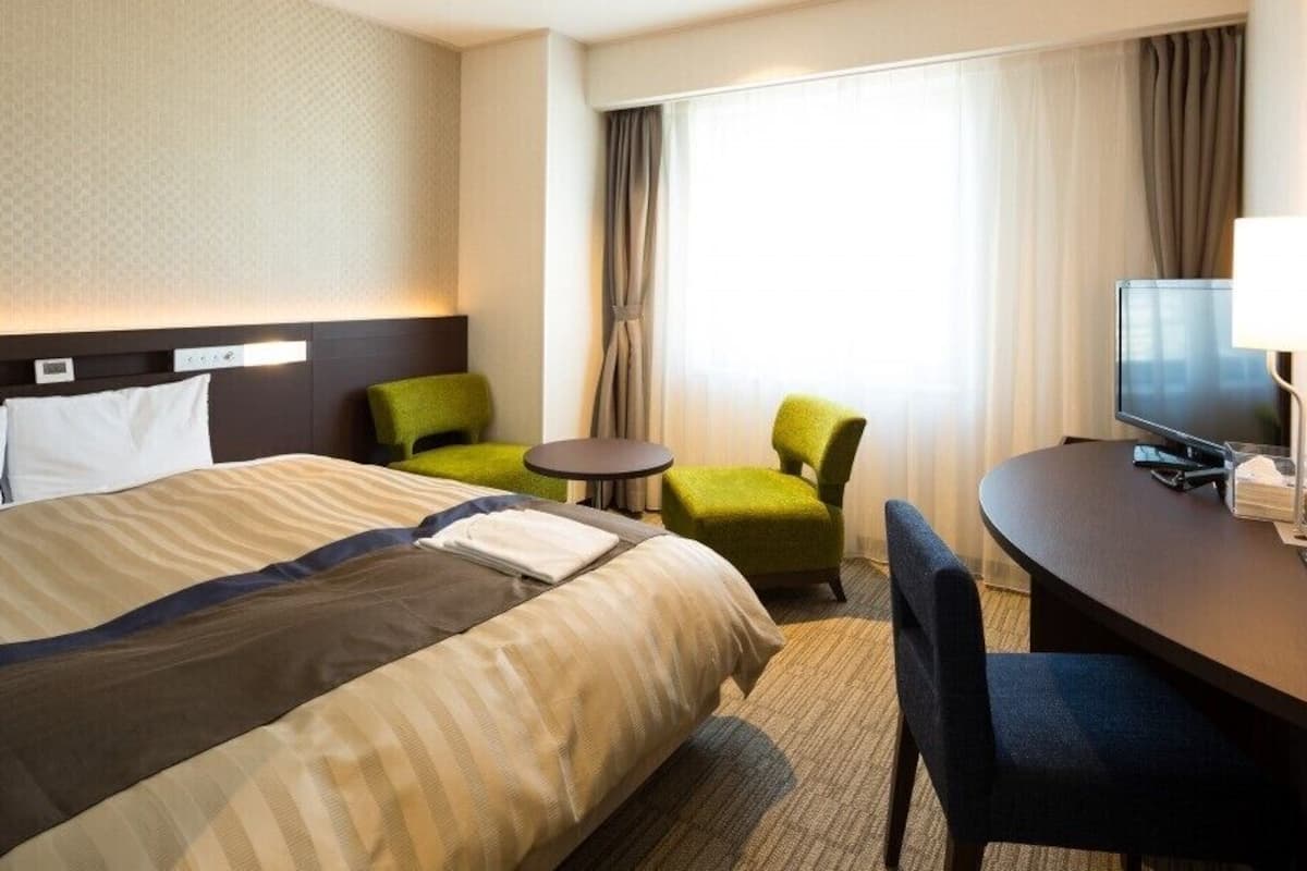 Ein Hotelzimmer mit einem Bett, einem Schreibtisch mit Stuhl, einem Fernseher und einem kleinen Tisch.