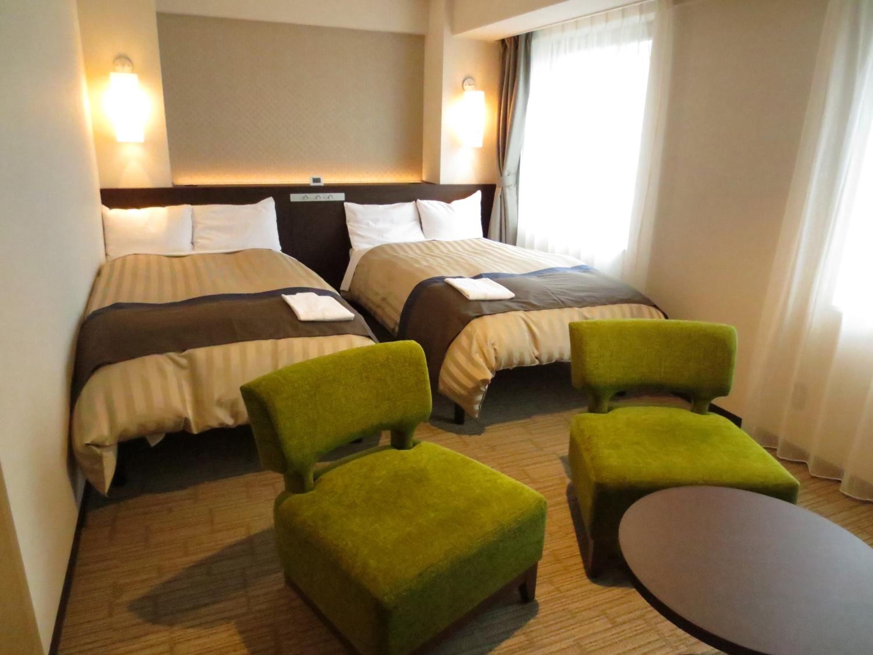 Habitació d'hotel amb dos llits, una taula petita i dues butaques verdes.