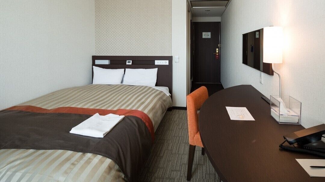 A hotel room with two beds, a desk, a chair, a lamp, and a mirror.