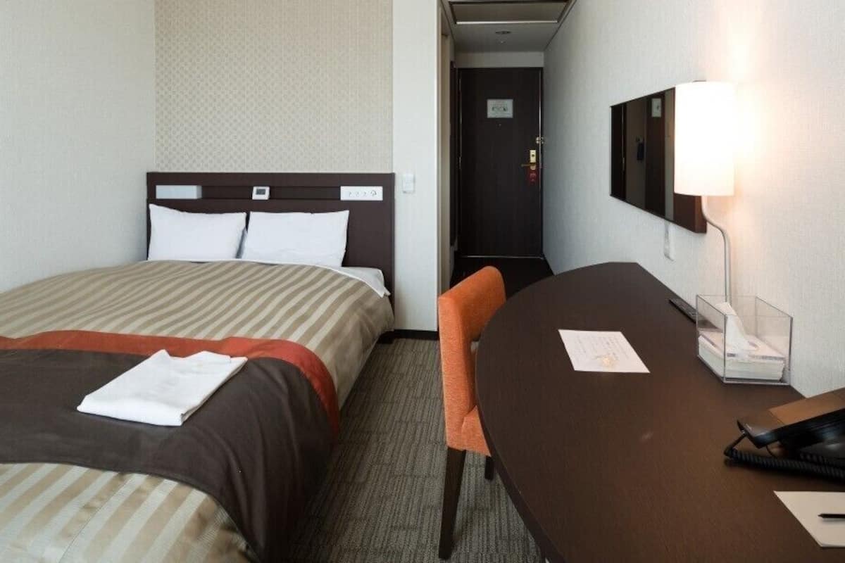 Ein Hotelzimmer mit zwei Betten, einem Schreibtisch, einem Stuhl, einer Lampe und einem Spiegel.