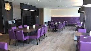 Uma área de refeições moderna com cadeiras e mesas roxas, um relógio na parede e piso de madeira.
