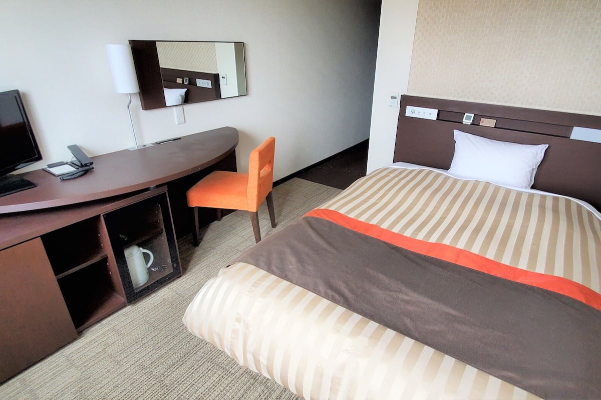 Ein Hotelzimmer mit Bett, Schreibtisch, Stuhl, Fernseher und Spiegel.