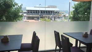 Restaurante com mesas, cadeiras, janelas amplas e vista para um edifício.