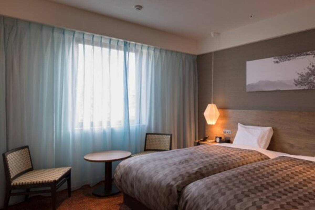 Una habitación de hotel con una cama grande, una pequeña mesa redonda, dos sillas, una mesita de noche con una lámpara y un cuadro en la pared.