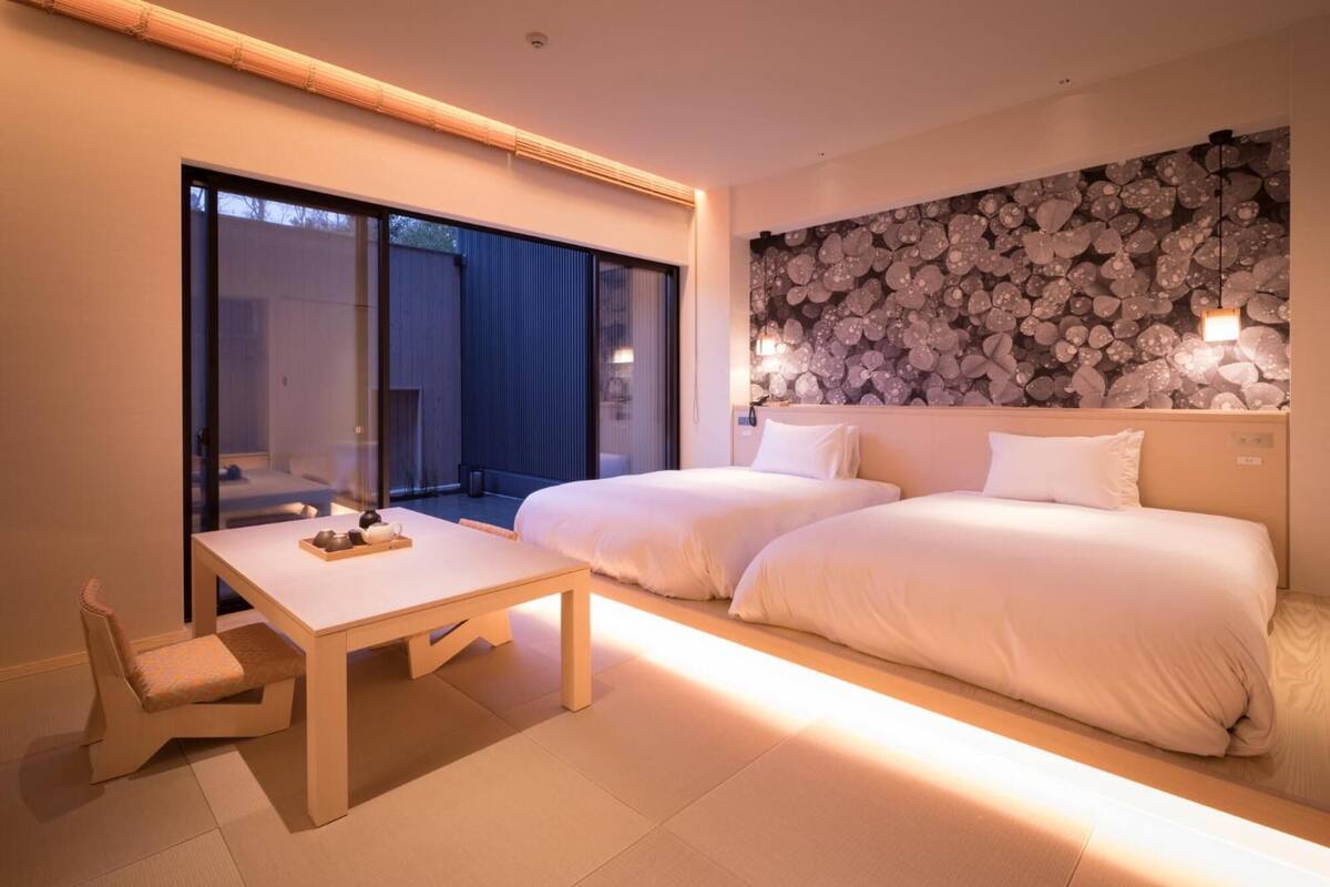 Una habitación de hotel moderna con dos camas, una mesita con una bandeja de objetos y un ventanal grande.