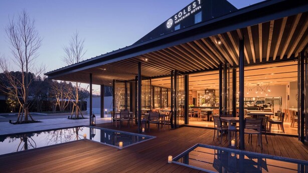 Un hôtel moderne doté d’un espace extérieur couvert, avec un sol en bois et des murs en verre.